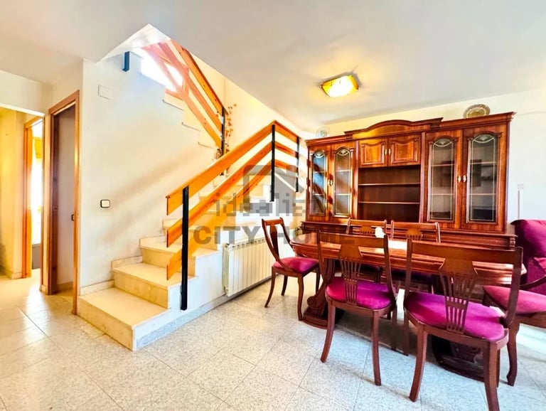 Modern living room with wooden staircase, dining table with pink chairs, and wood cabinet furniture along the wall