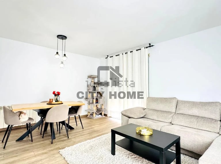 Modern open-plan living room with beige sofa, dining table, chairs, and wooden flooring in a bright apartment