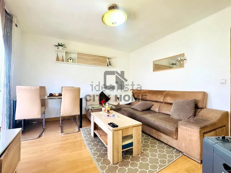 Compact apartment living room with beige sofa, dining chairs, wooden coffee table, and light wood floating shelves