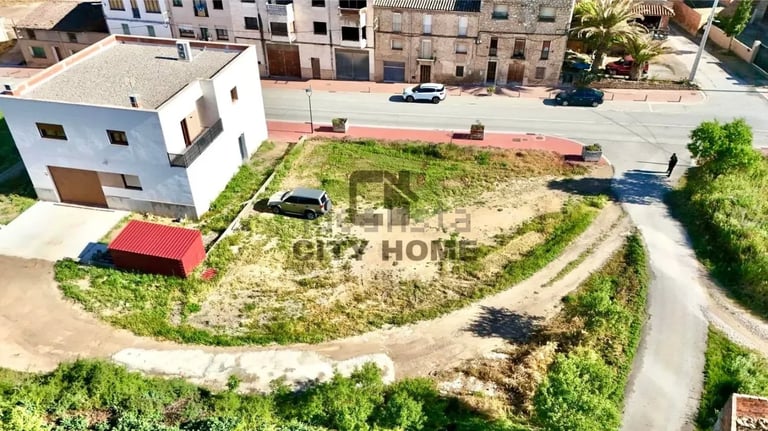 Aerial view of a residential lot with a white house, red shed, parked cars, and grassy surroundings bordered by neighboring buildings