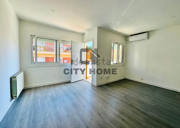 Empty modern apartment with mixed hardwood flooring, white walls, windows, air conditioning unit, and glass door