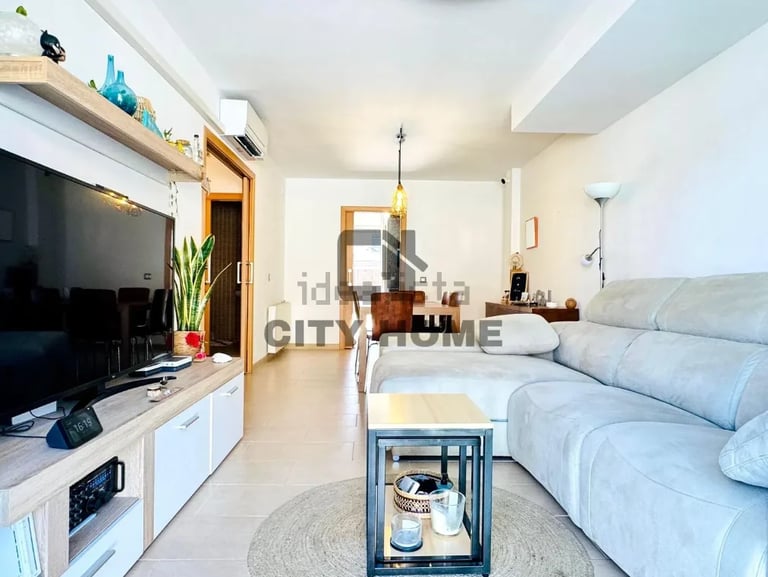 Modern open-plan living room with light blue sectional sofa, wall-mounted TV, wooden shelving, and minimalist décor