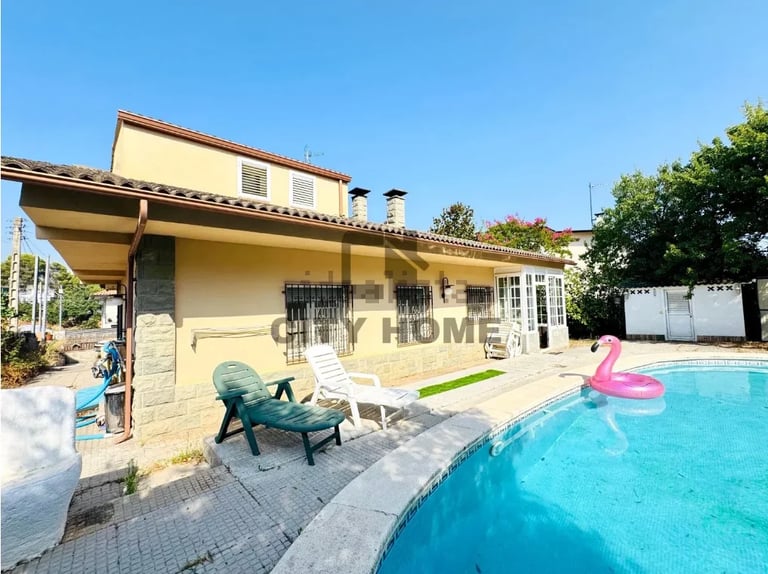 Modern two-story cream and stone house with pool, lounge chairs, and palm floatie on a sunny day