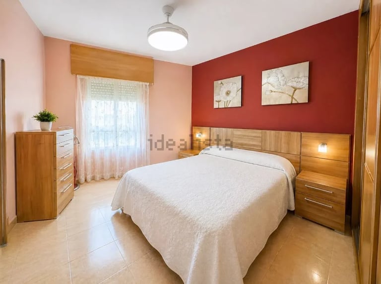 Modern bedroom with wooden furniture, red accent wall, and white bedding